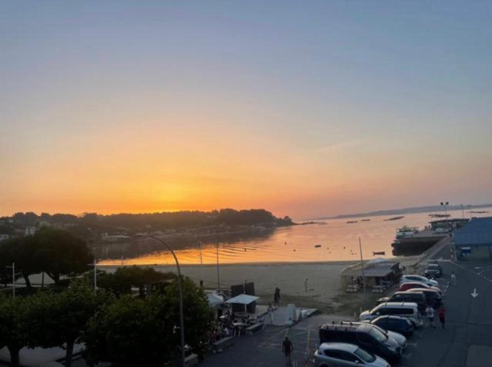 grupa samochodów zaparkowanych na plaży o zachodzie słońca w obiekcie CRUZAS LA CALLE Y ESTAS EN LA PLAYA w mieście Bueu