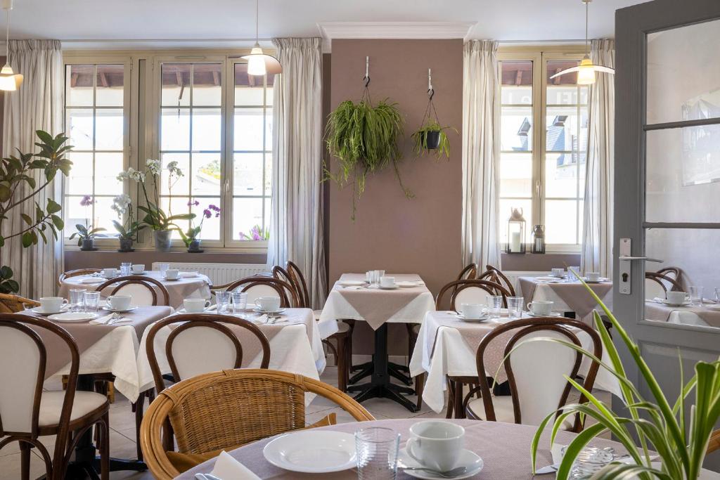 a restaurant with white tables and chairs and windows at Hôtel de Lion sur Mer in Lion-sur-Mer