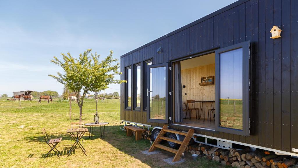 ein schwarzes Haus mit Fenstern, einem Tisch und Bänken in der Unterkunft Tiny House haras Normand - 20 minutes d'Étretat 