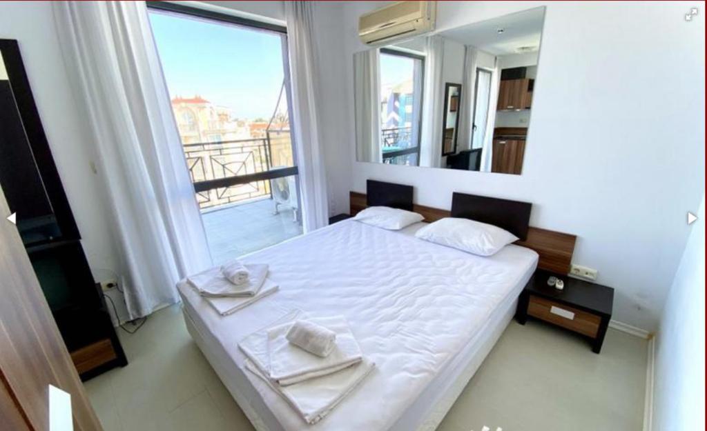 a bedroom with a white bed with a large window at Rainbow 3 Sunny Beach Topo Apartment in Sunny Beach