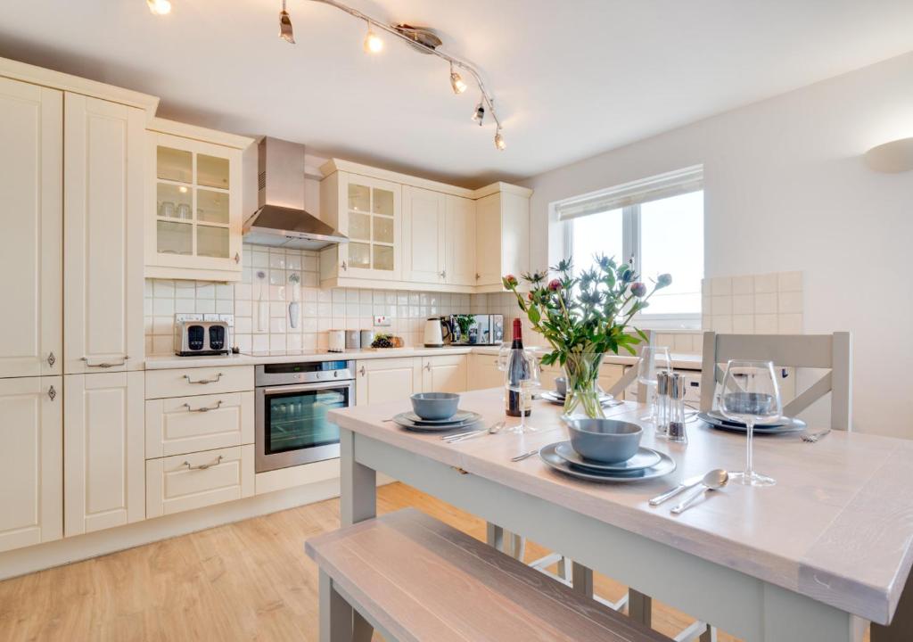 a kitchen with white cabinets and a table with flowers on it at Loveday in Porthleven