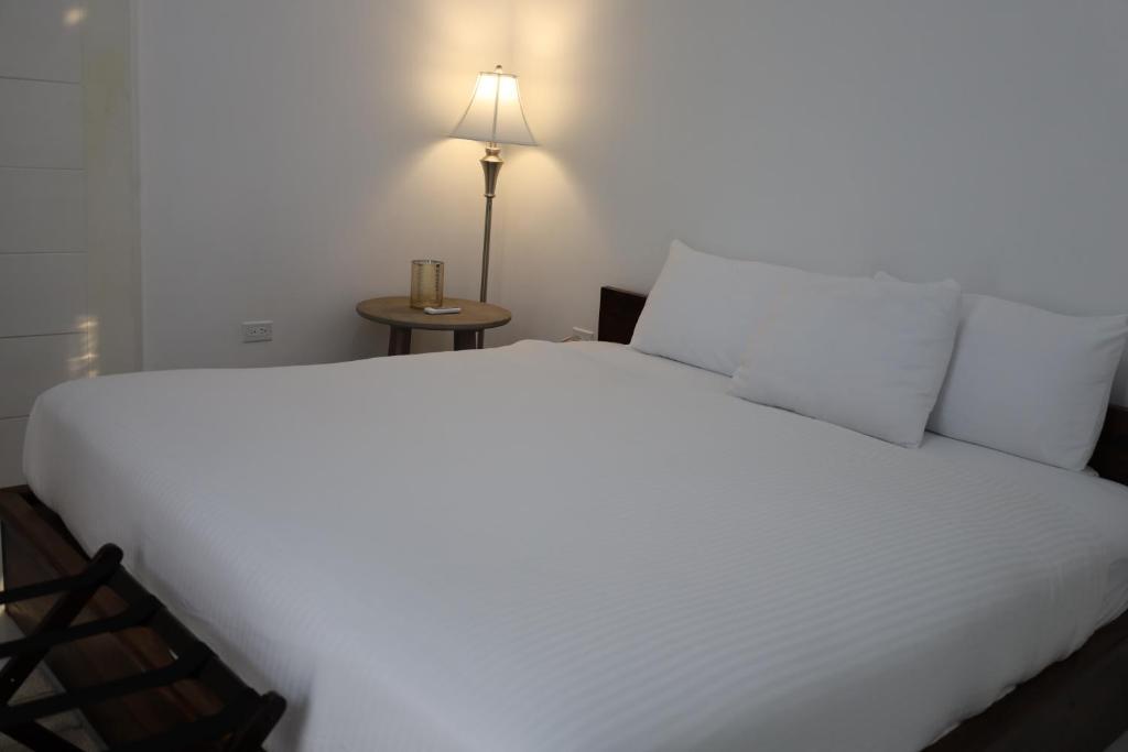 a bedroom with a large white bed with a lamp at The Ellysian Apartments in Placencia Village