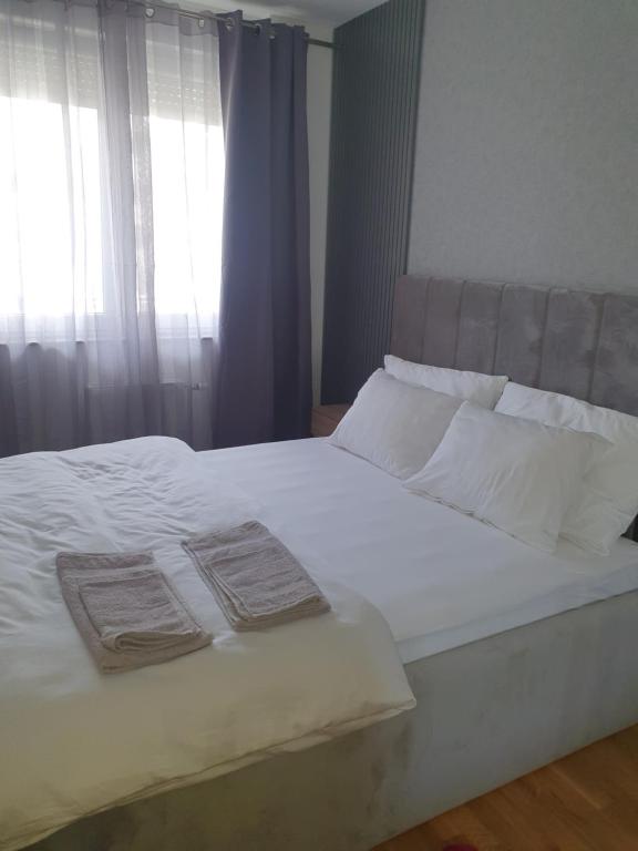 uma cama com lençóis e almofadas brancos e uma janela em Sajam 1 em Novi Sad
