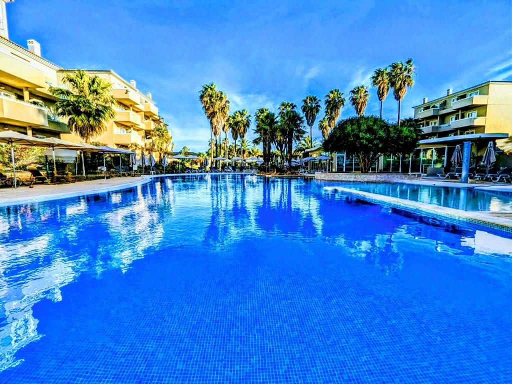 a large swimming pool with blue water and palm trees at VilaBplaza by JohnVillas in Alvor