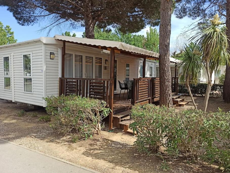 a white cabin with a porch and a tree at Mobil-home FO 88 à VIAS in Vias