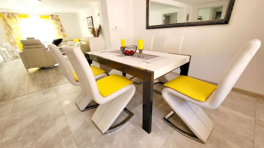 une table à manger avec des chaises blanches et des coussins jaunes dans l'établissement Carpe Diem Lakeside Apartment, à Szczecin