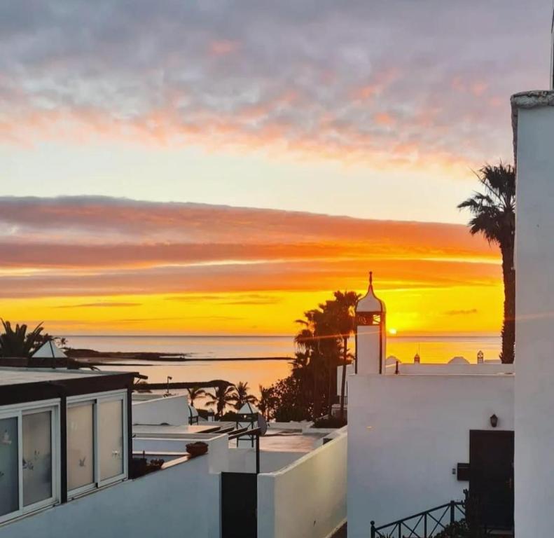 zachód słońca nad oceanem z budynkiem i wieżą zegarową w obiekcie Cozy Waterman beach house w Costa Teguise