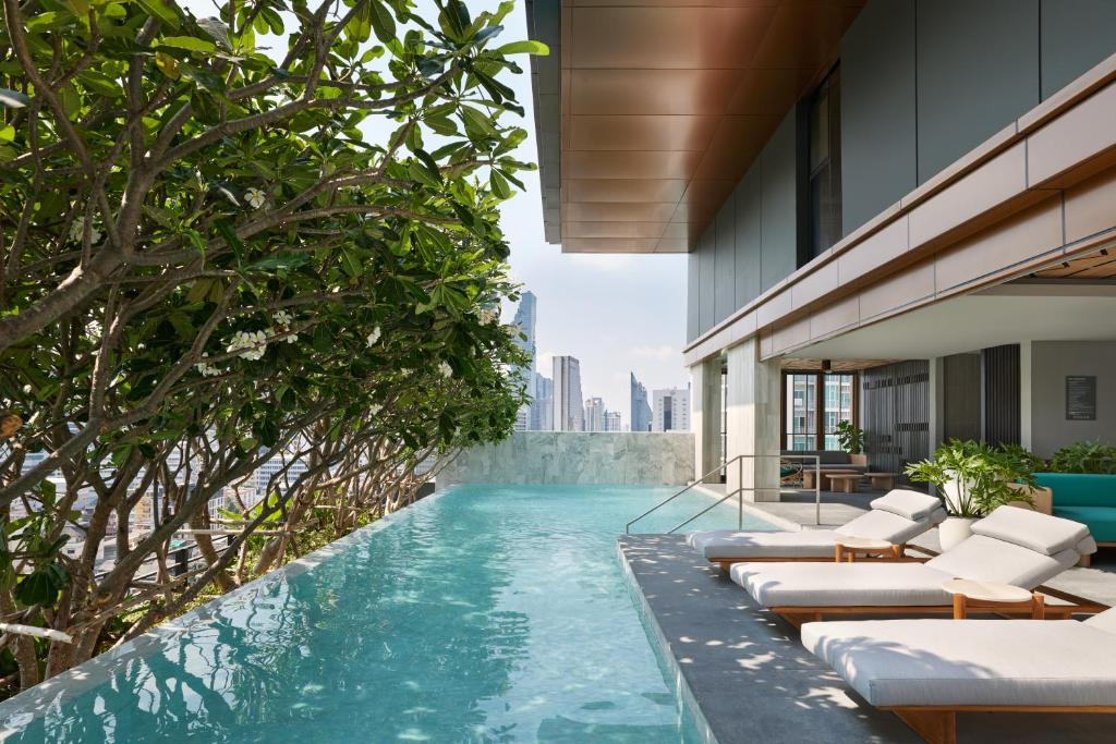 A narrow rooftop-style infinity pool lined with loungers and framed by Bangkok towers.