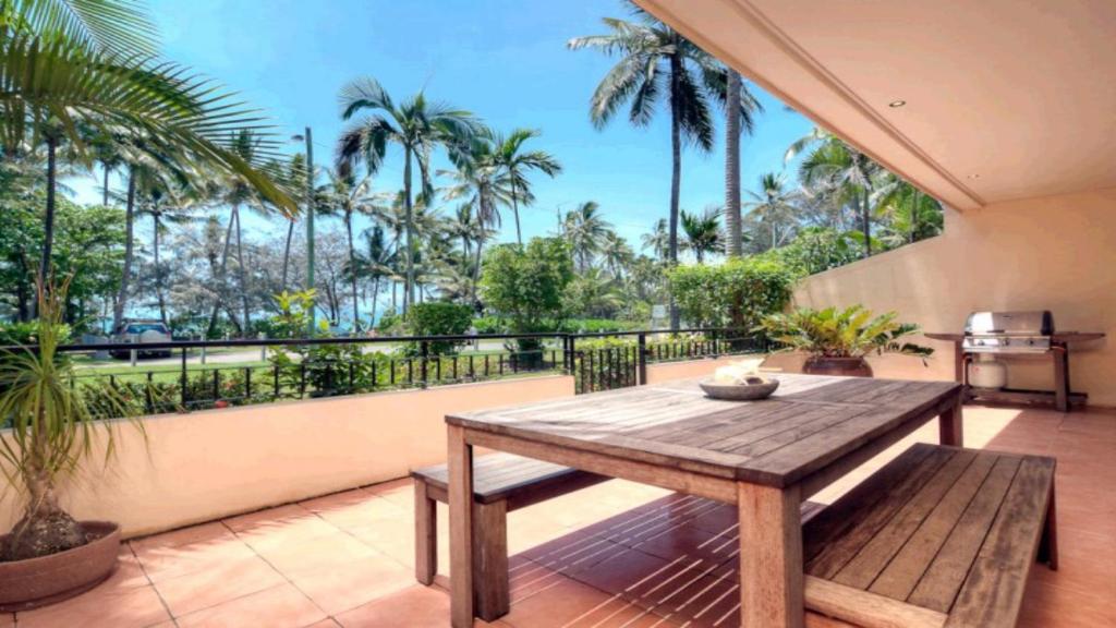 uma mesa de madeira e banco numa varanda com palmeiras em On The Beach 3 Port Douglas em Port Douglas