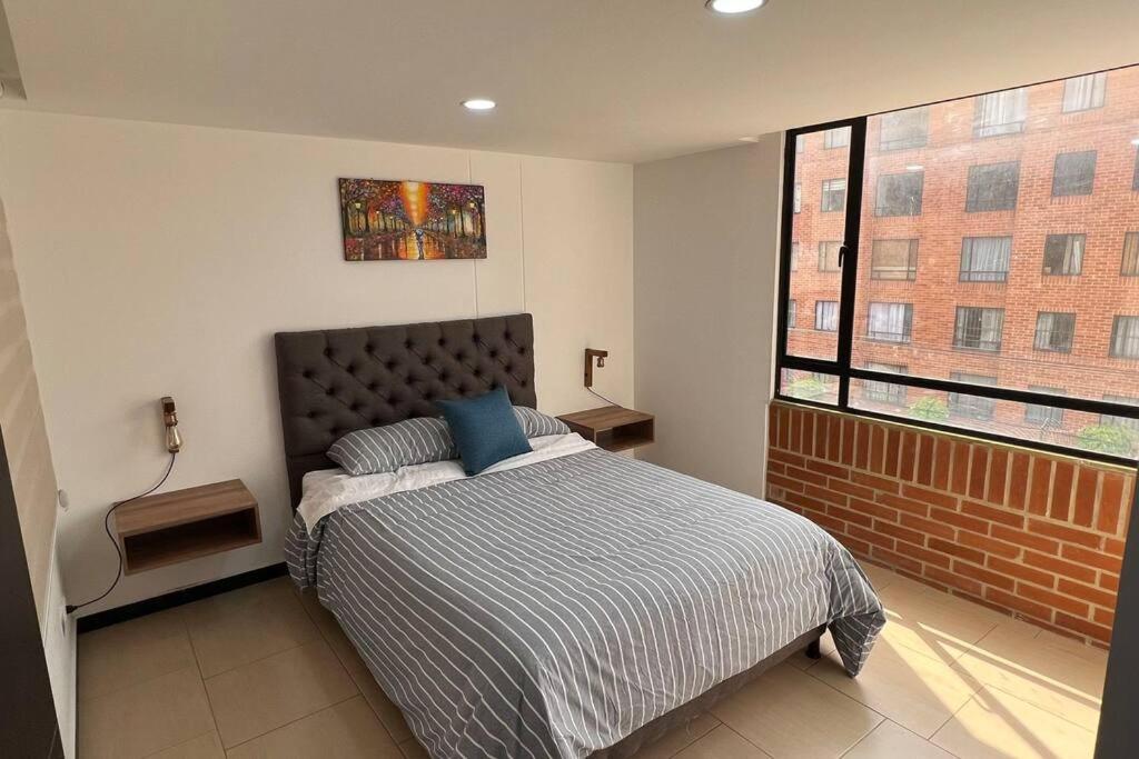 ein Schlafzimmer mit einem Bett und einem großen Fenster in der Unterkunft Encantador apartamento cerca al aeropuerto in Bogotá