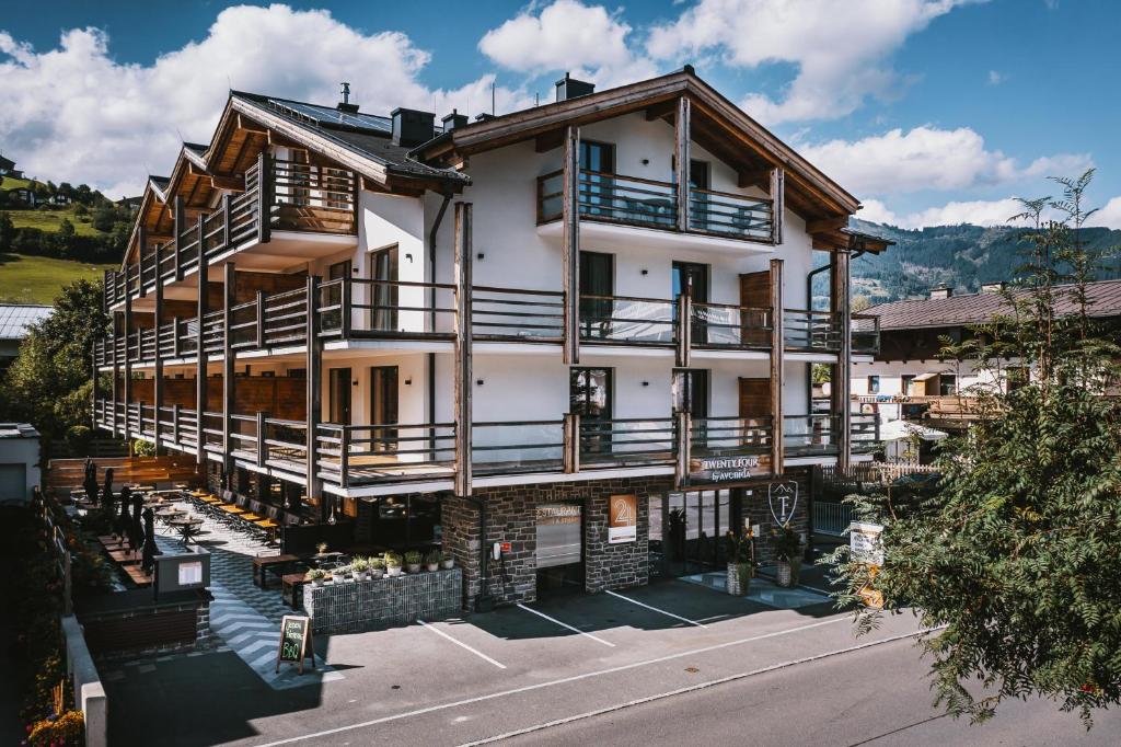 Un grand bâtiment blanc avec des balcons en bois se trouve dans une rue. dans l'établissement 24 by AvenidA - Mountain Hotel, à Kaprun