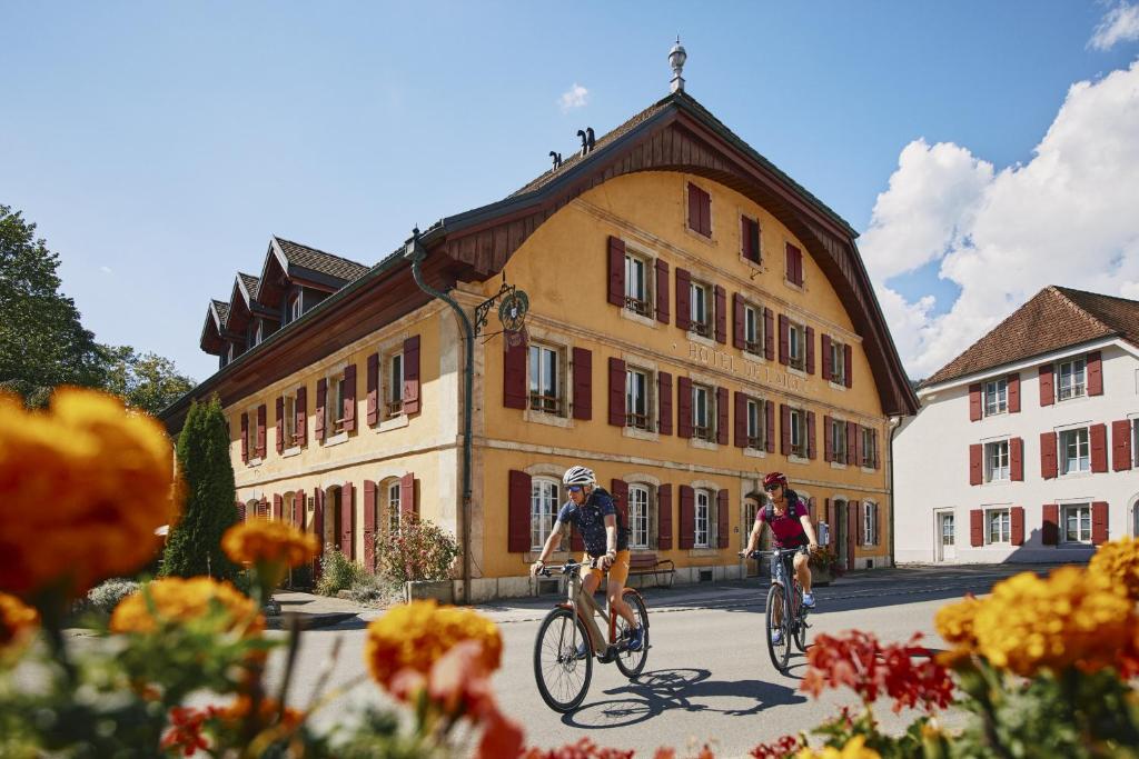 dwoje ludzi jeżdżących rowerami przed budynkiem w obiekcie Hôtel de l'Aigle w mieście Couvet