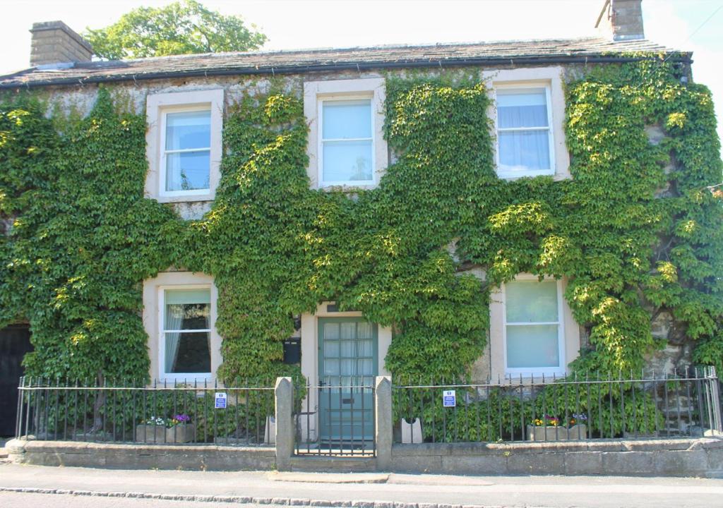 an ivy covered house with a fence in front of it at Kingston House in West Witton