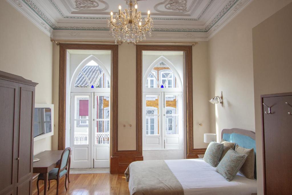 a bedroom with a bed and a chandelier and two windows at Dom José Alojamentos by Guestify in Guimarães