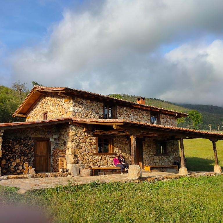 a stone house in a field with people sitting in front of it at Invernal de Tobaño in Cahecho