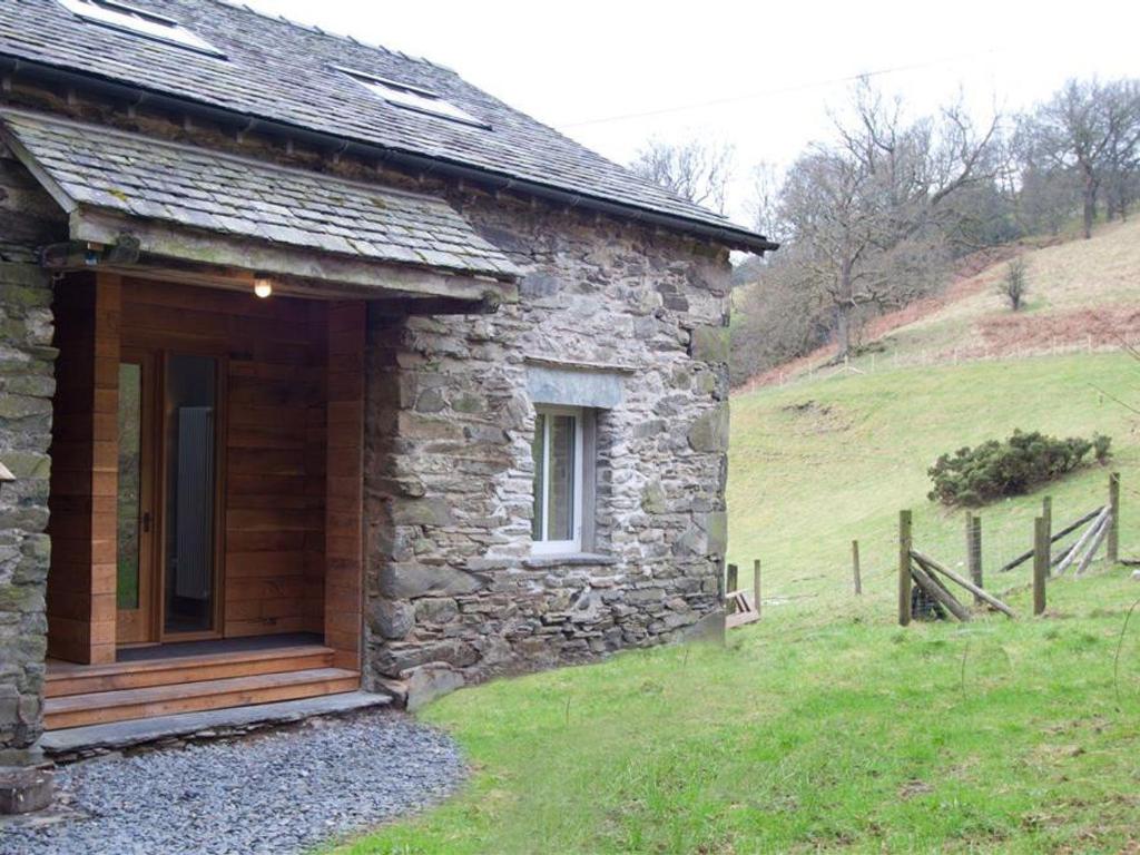 a stone house with a wooden door in a field at Sunny Brow Hayloft in Ambleside