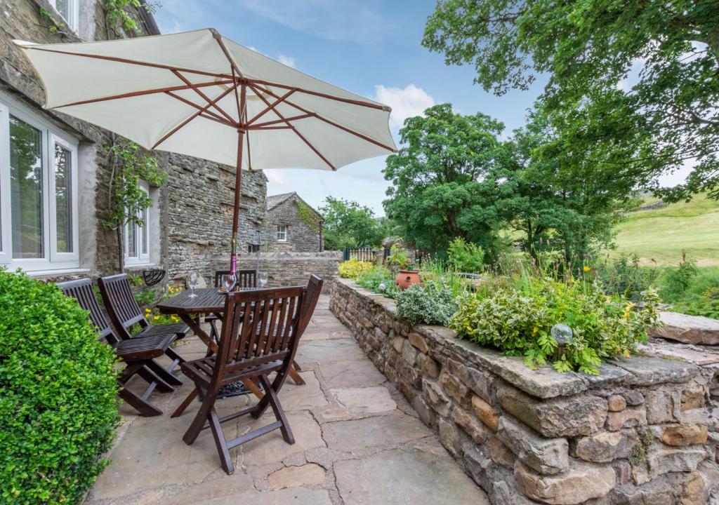 a table and chairs with an umbrella on a stone wall at Foss Garth Cottage in Thwaite