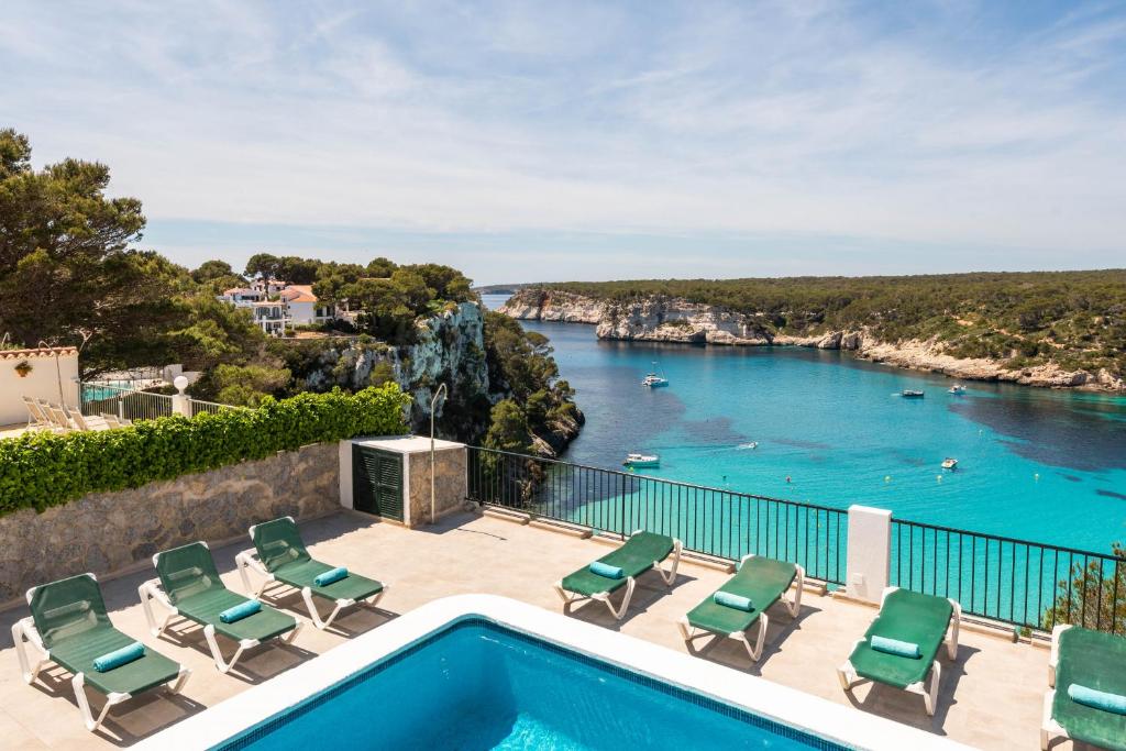 einen Pool mit Stühlen und Blick auf das Wasser in der Unterkunft Villa Vista Alegre - Cala Galdana in Ferreries