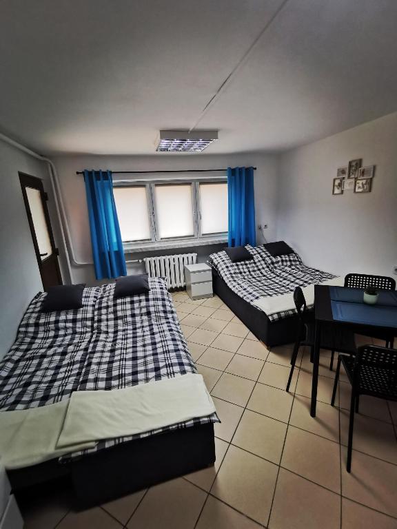 two beds in a room with blue curtains and a table at Wyspani Zator in Zator