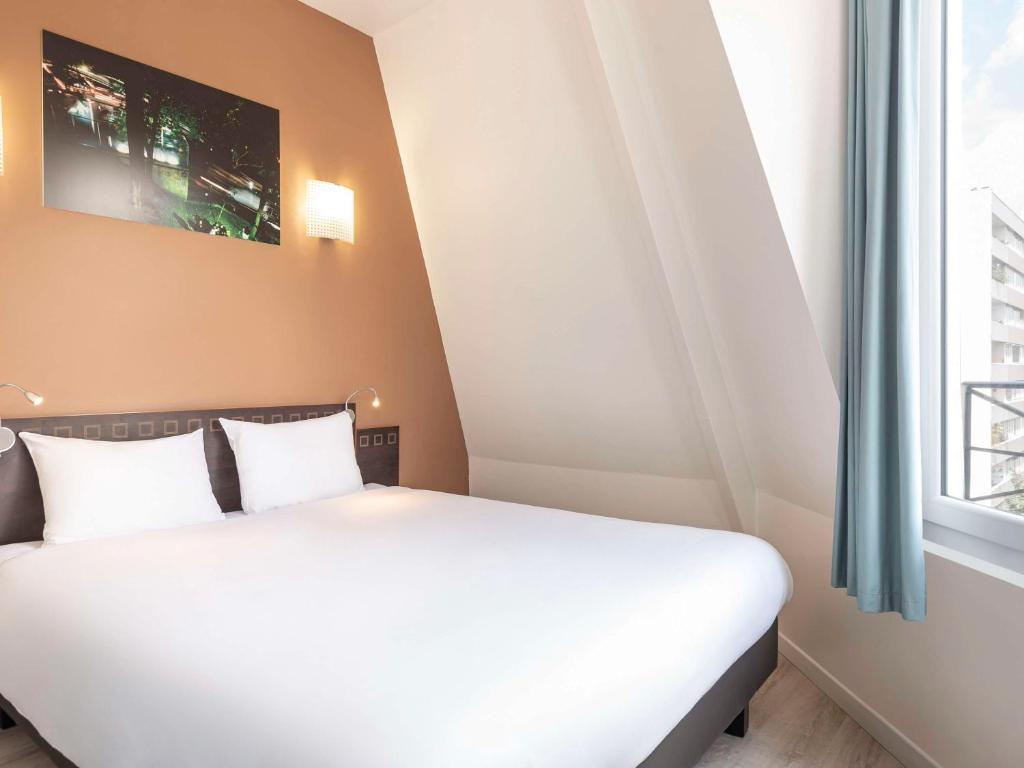 sypialnia z białym łóżkiem i oknem w obiekcie Aparthotel Adagio Access Paris Philippe Auguste w Paryżu