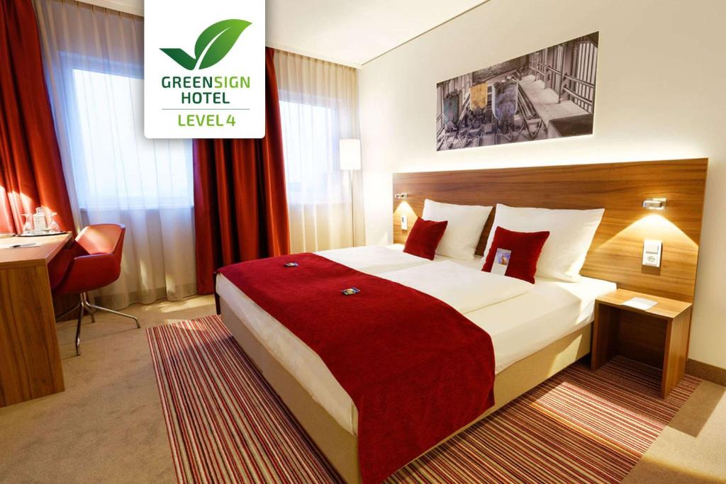 a hotel room with a large bed with a red blanket at GHOTEL hotel & living Essen in Essen