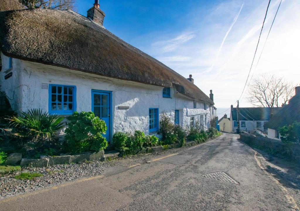 an old white cottage with a thatched roof on a road at Renes Cottage in Ruan Minor