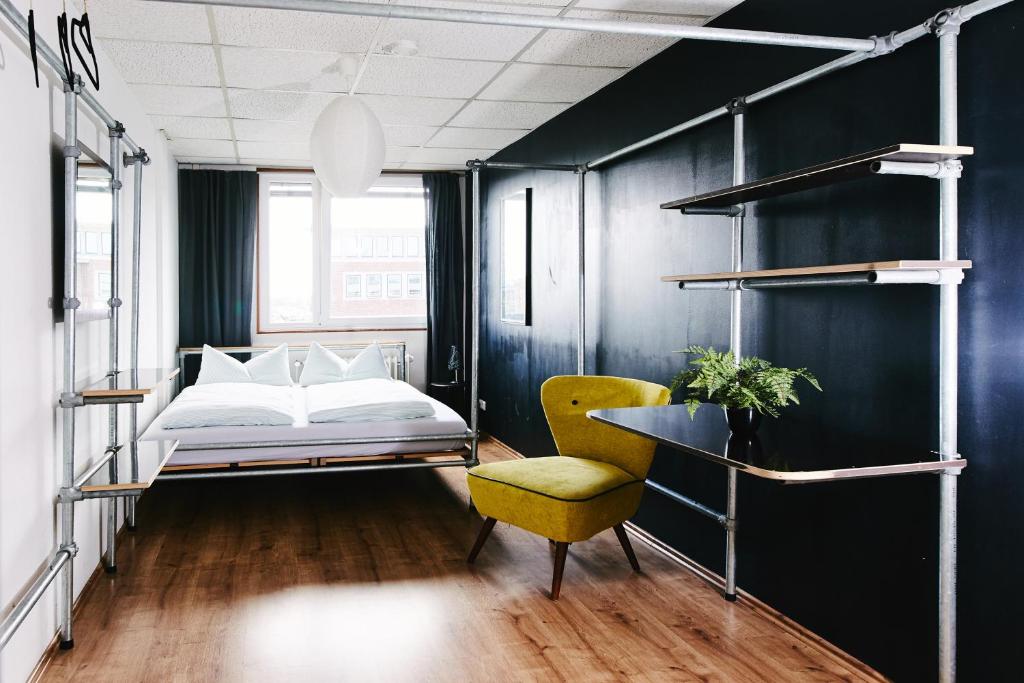 a bedroom with a bed and a yellow chair at Sleep Station Hostel in Münster