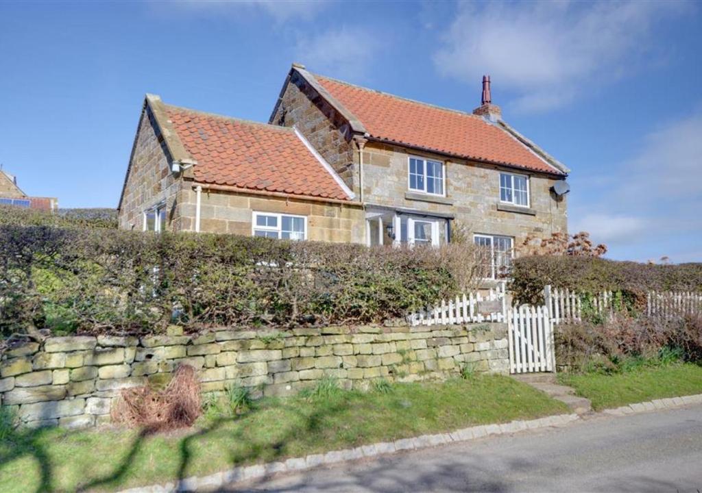 a house with a stone wall and a fence at Cheyne Cottage in Hawsker