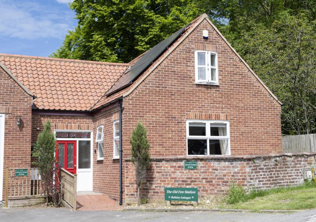 een oud bakstenen gebouw met een rode deur en een bord bij Call Out Cottage in Sledmere