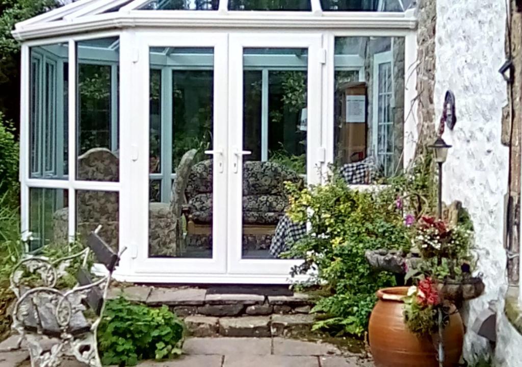 a conservatory with a white door and some plants at Buttercup Cottage in Tosside