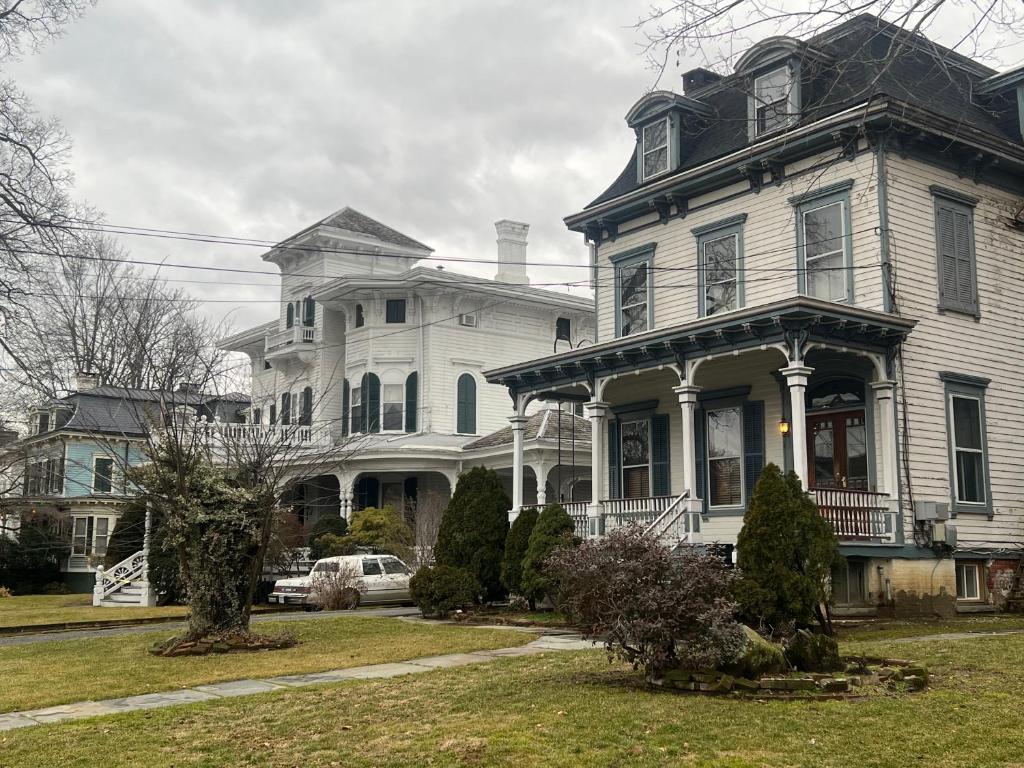 une grande maison blanche avec une véranda dans une rue dans l'établissement Private Victorian Apartment in convenient City location on 5 acre, Sleeps 5, à Poughkeepsie