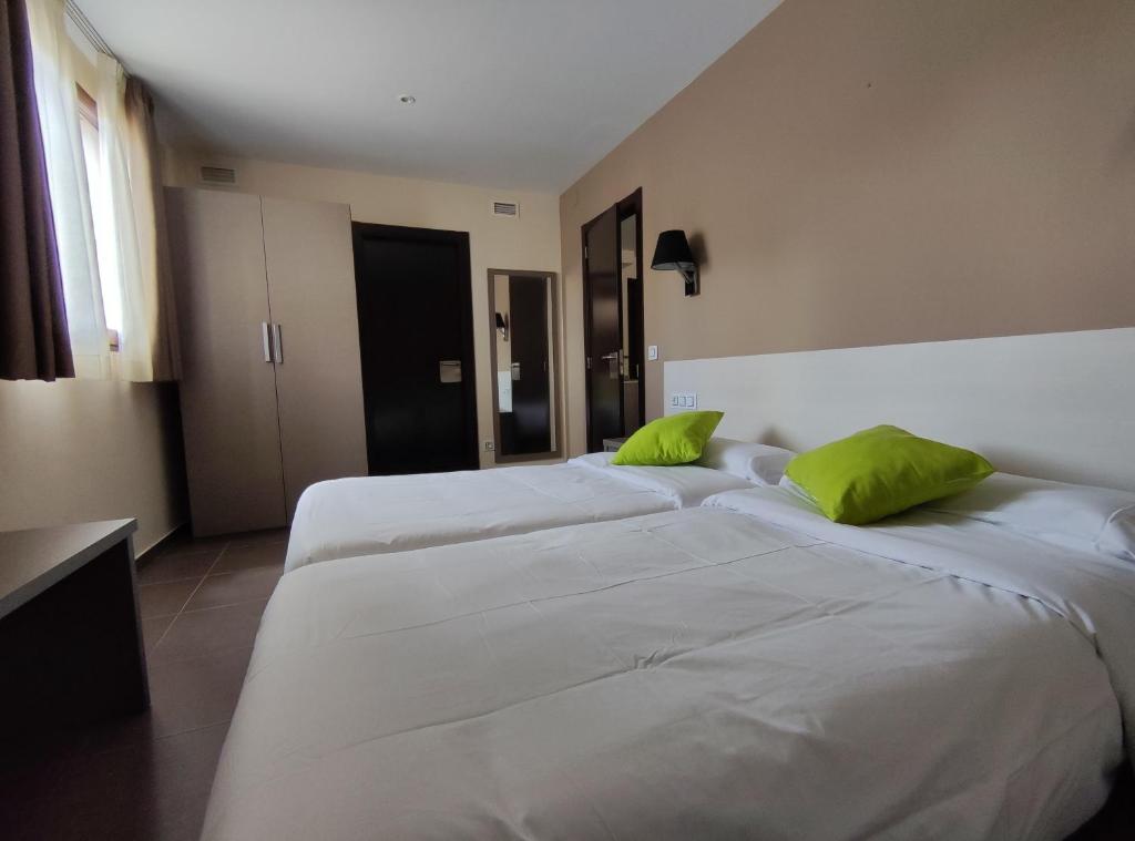 Aparthotel Castellfort في Castellfort: سريرين في غرفة الفندق مع وسائد خضراء