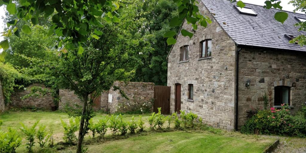 an old stone house with a tree in the yard at Cosy two bedroom lodge on the edge of Raheen Woods in Tuamgraney