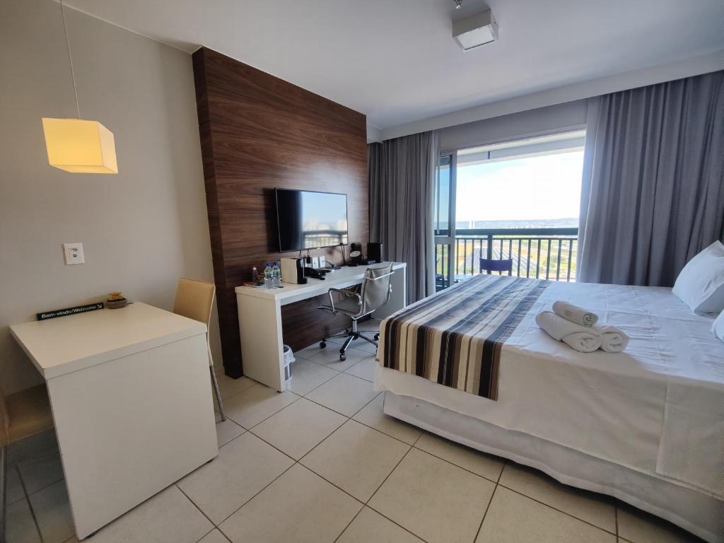 a hotel room with a bed and a desk and a window at Vision otima localização vista incrível e muitas comodidades in Brasilia