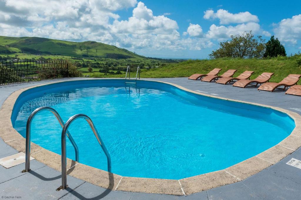 a swimming pool with chairs and blue water at Farmhouse & exclusive outdoor heated pool in Bryn-crug