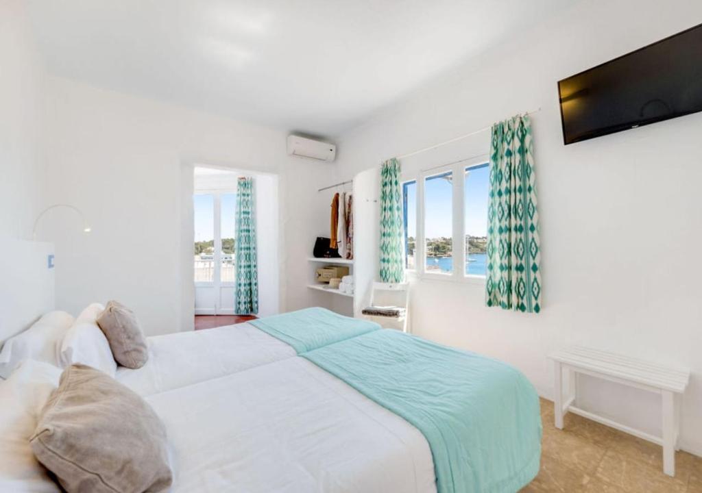 a white bedroom with a bed and two windows at Hotel Baluma Porto Petro in Portopetro