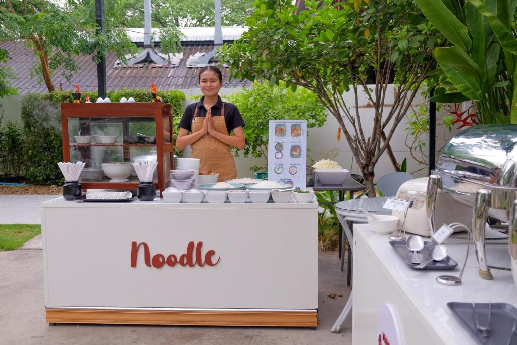 a woman standing in front of a table with aania sign at Tree Tara hotel in Lampang