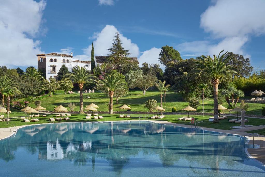 a pool with palm trees and a building in the background at La Bobadilla, a Royal Hideaway Hotel in Villanueva de Tapia