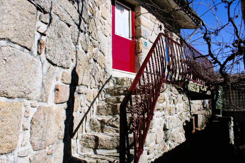 um edifício de pedra com uma janela vermelha e uma escada em Casa da Cuca em Campo do Gerês