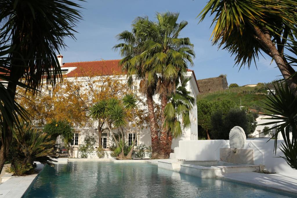 a swimming pool with palm trees in front of a building at Pateo dos Solares Charm Hotel in Estremoz