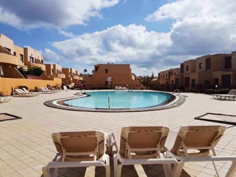 two chairs and a swimming pool in a courtyard with buildings at Piscina & Wifi. SUNNY apartement, swimming pool. in Caleta De Fuste