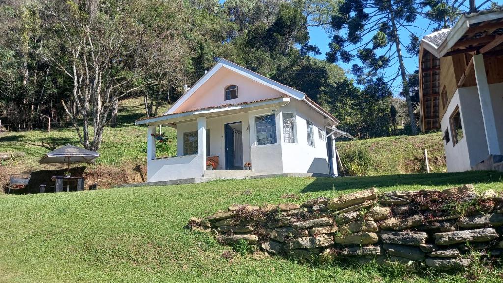 a small white house with a stone wall at Chalé doce beija-flor in Campos do Jordão