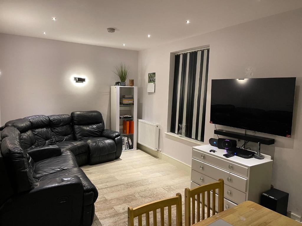 a living room with a black leather couch and a flat screen tv at Crossbrook street in Cheshunt