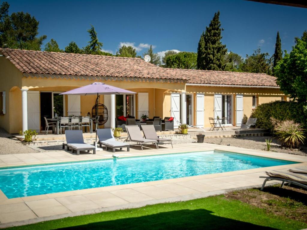 a pool with chairs and an umbrella next to a house at Loustalet in Bagnols-en-Forêt