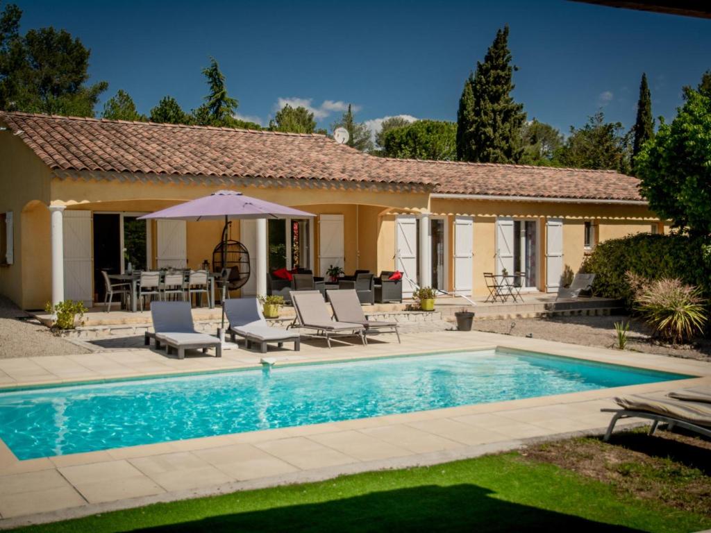 een zwembad met stoelen en een parasol naast een huis bij Loustalet Plus in Bagnols-en-Forêt