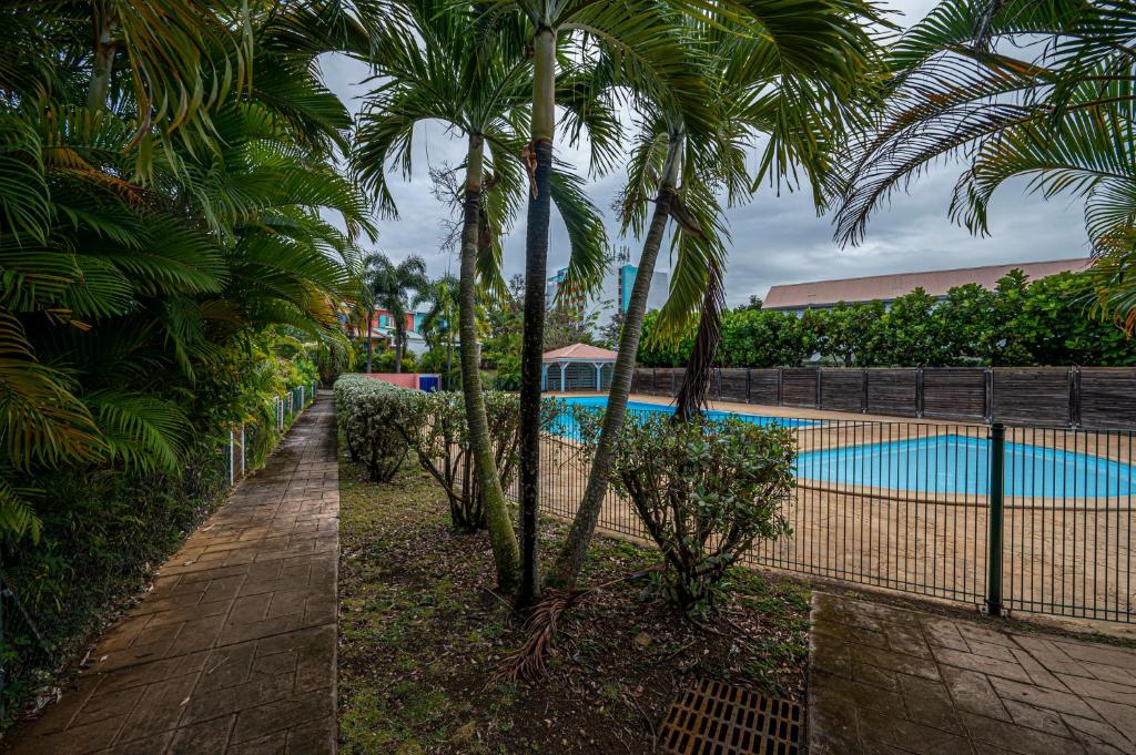 a pool with palm trees next to a fence at Rêve de Palmier in Le Gosier