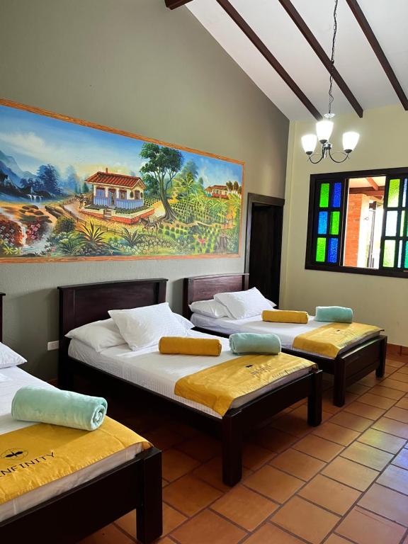 Habitación con 3 camas y una pintura en la pared. en Hotel Campestre Los Mangos, en Quimbaya