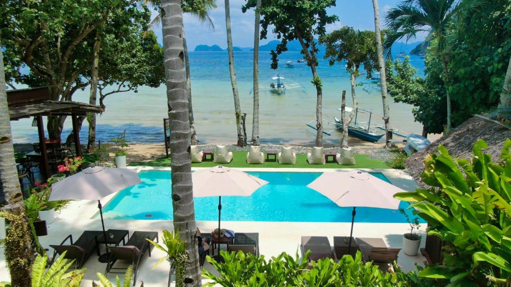 a swimming pool with chairs and umbrellas next to the ocean at Last Frontier Beach Resort-Adults Only in El Nido