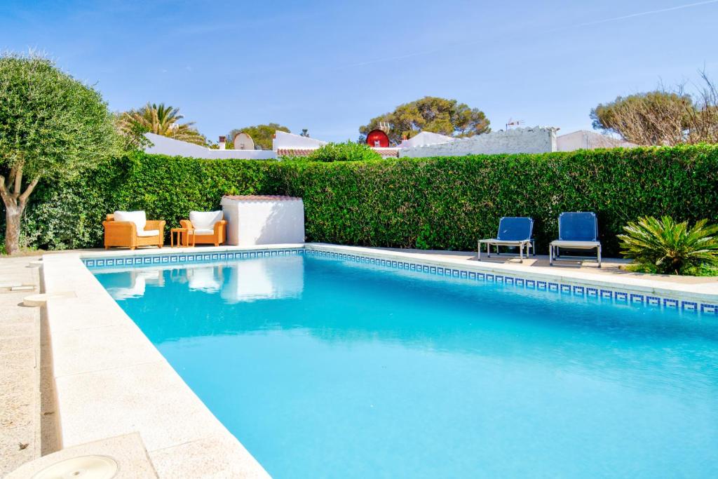 a swimming pool with two blue chairs and bushes at Cas Buc - Villa con piscina a pasitos del mar in Cala Blanca