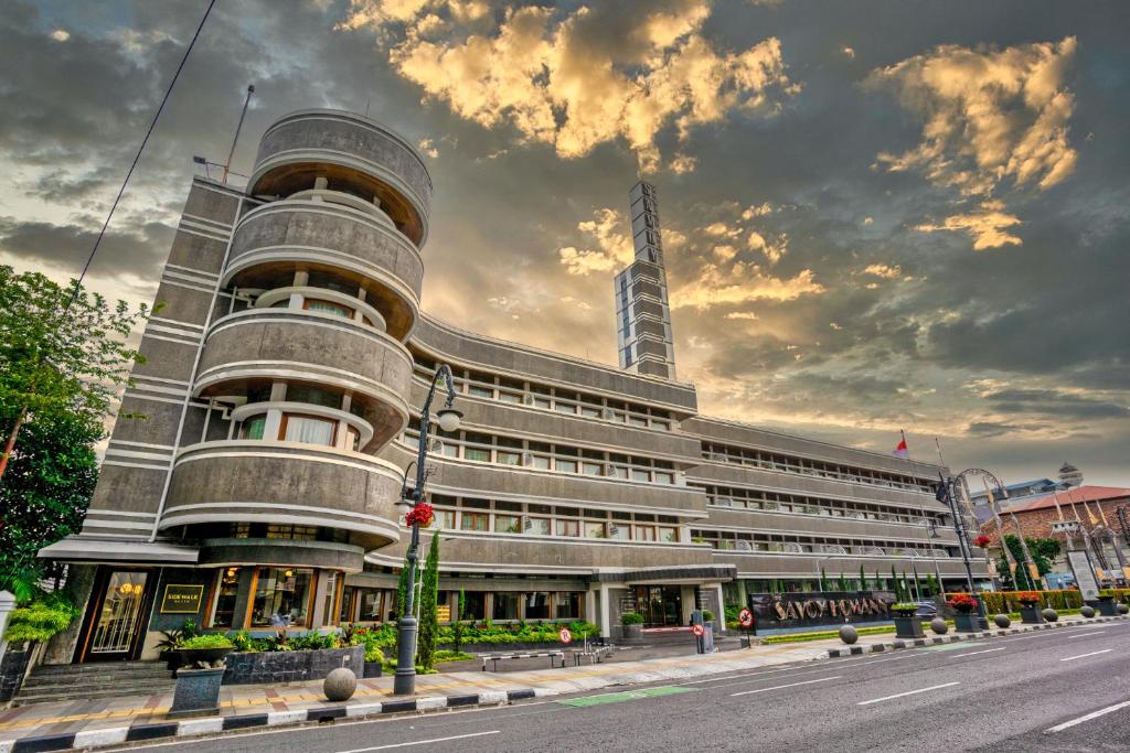 een groot gebouw in een stadsstraat met een bewolkte hemel bij Hotel Savoy Homann in Bandung